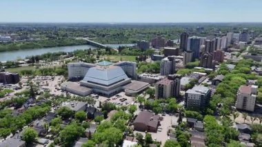 Şehir manzaralı, merkezinde büyük bir bina var. Şehir hareketlilikle dolup taşıyor. Gökyüzü açık ve güneş parlıyor.