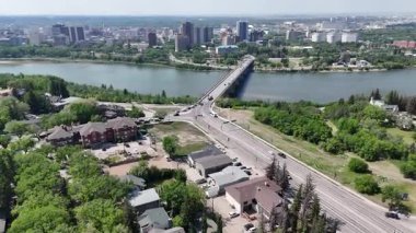 Şehir manzarası ve içinden bir nehir geçiyor. Şehir binalar ve arabalarla dolu. Sahne meşgul ve hareketli.