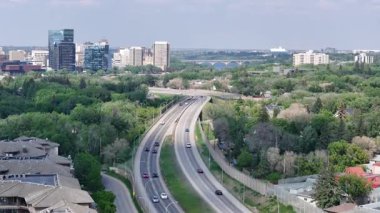Arka planda otoyol olan bir şehir. Otoyol arabalar ve kamyonlarla dolu. Şehir yüksek binalar ve ağaçlarla dolu.