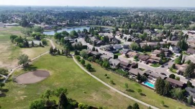 Park ve yüzme havuzu olan bir yerleşim yeri. Evler dağıldı ve caddeye park edilmiş bir sürü araba var.