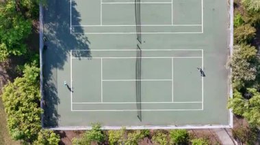 Tenis kortunda iki kişi tenis oynuyor. Saray ağaçlar ve çalılarla çevrili. Manzara huzurlu ve rahatlatıcı.