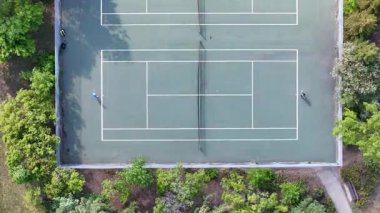 Tenis kortunda iki kişi tenis oynuyor. Saray ağaçlar ve çalılarla çevrili. Manzara huzurlu ve rahatlatıcı.