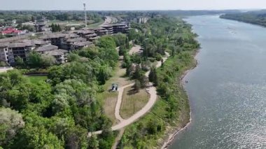 Üzerinde bir patika akan bir nehir manzarası. Yol ağaçlarla kaplı ve arka planda evler görülebiliyor.