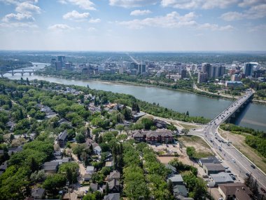 Şehir manzarası ve içinden bir nehir geçiyor. Şehir evler ve binalarla dolu. Gökyüzü mavi ve güneş parlıyor.
