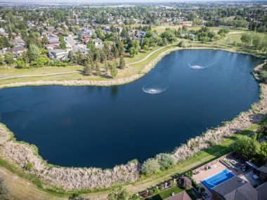 Etrafında yeşil çimenlik bir alan olan büyük bir su kütlesi. Su sakin ve berrak ve gölün ortasında iki çeşme var. Huzurlu ve huzurlu bir sahne.