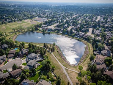 Ortasında büyük bir gölet olan yerleşim yeri manzarası. Gölet evler ve ağaçlarla çevrili.