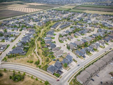 Evleri ve caddeleri olan bir yerleşim yeri. Evlerin çoğu beyaz ve caddeye park etmiş birkaç araba var.