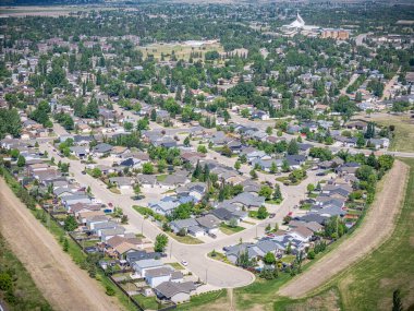 Evleri ve ağaçları olan bir yerleşim yeri. Evlerin çoğu beyaz ve caddeye park edilmiş bir sürü araba var.