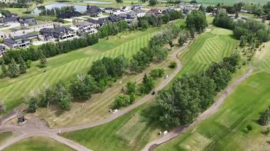 Arka planda birkaç ağaç ve ev olan golf sahası. Golf sahası boş ve çimenler yeşil.