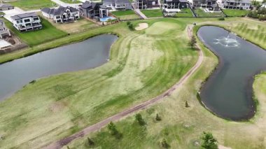 Göllü golf sahası ve arka planda evleri var. Golf sahası çitlerle çevrili ve yeşil çimenli bir alanı var.