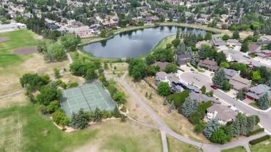 Tenis kortu ve göleti olan bir park. Gölet ağaçlar ve evlerle çevrilidir. Park boş ve huzurlu.