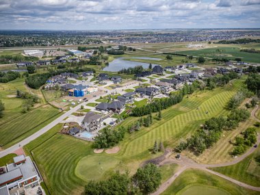 Arka planda evleri olan golf sahası. Evler dağılmış durumda ve civarda birkaç ağaç var.