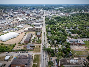Arka planda beyaz bir bina olan şehir caddesi. Sokaklar ağaçlar ve evlerle dolu.