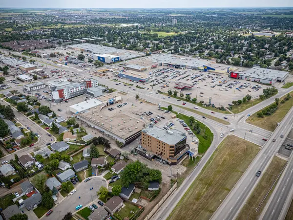 Arka planda büyük bir alışveriş merkezi olan şehir caddesi manzarası. Alışveriş merkezi araba ve insanlarla dolu ve birkaç trafik ışığı görünüyor. Sahne meşgul ve hareketli.