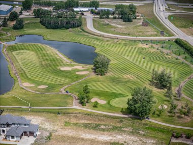 Arka planda göleti ve evi olan bir golf sahası. Golf sahası bakımlı ve huzurlu bir atmosferi var.