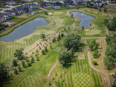 Arka planda ağaçlar ve gölcüklü golf sahası. Golf sahası evlerle çevrili.