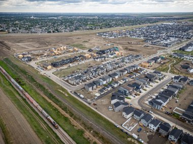Birçok evi olan bir yerleşim bölgesinden tren geçiyor. Tren görüntünün solunda ve evler de sağda.