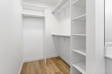 Ahşap zemini ve beyaz rafları olan küçük beyaz bir dolap. Dolap boş ve oda çok temiz.