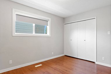 Penceresi ve dolabı olan beyaz bir oda. Oda boş ve minimalist bir görünüşü var.