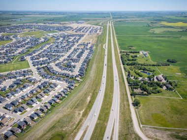 Yolun iki tarafında da evler var. Evlerin çoğu beyaz ve birkaç kahverengi ev var. Yol boş, birkaç araba hariç.