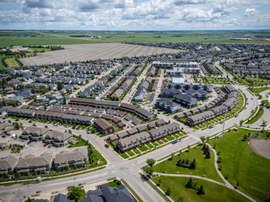 Evleri ve parkı olan bir yerleşim yeri. Evlerin çoğu beyaz ve kahverengi. Sokakta birkaç araba var.