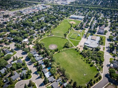 Büyük yeşil bir arazisi ve arka planda birkaç evi olan bir park. Park bir çitle çevrili ve birkaç bankı var.