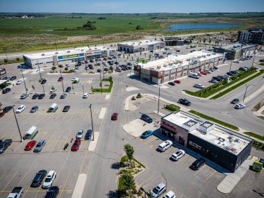 Bir sürü park yeri ve mağazası olan yoğun bir alışveriş merkezi. Gökyüzü mavi ve güneş parlıyor.