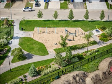 Oyun parkı ve bankı olan bir park yeri. Park ağaçlarla çevrili ve çitleri var.