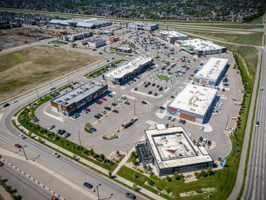 Bir sürü park yeri olan büyük bir alışveriş merkezi. Alışveriş merkezi çimenli bir alanla çevrilidir ve birkaç ağacı vardır. Otoparkta park etmiş bir sürü araba var ve bazıları yolda gidiyor.