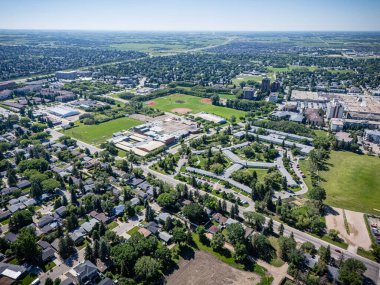 Ortasında park olan şehir manzarası. Park evler ve binalarla çevrilidir. Gökyüzü açık ve güneş parlıyor.