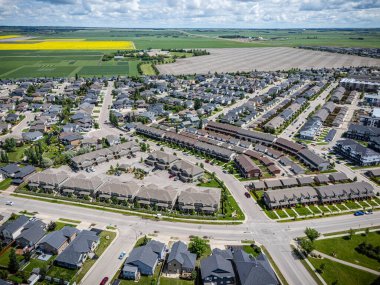 Evleri ve birkaç arabası olan bir yerleşim yeri. Evlerin çoğu beyaz ve kahverengi. Sokaklar ağaçlarla kaplı ve gökyüzü bulutlu.