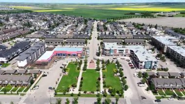 Solunda büyük bir bina ve sağında daha küçük bir bina olan şehir caddesi. Sokaklar ağaçlar ve evlerle dolu.