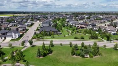 Ortasında çit olan büyük yeşil bir alan. Tarla evler ve ağaçlarla çevrili.