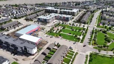 Ev ve dairelerin karışımı olan bir yerleşim yeri. Evler çoğunlukla beyaz ve daireler çoğunlukla kırmızı. Sokak ağaçlarla dolu ve cadde boyunca park edilmiş birkaç araba var.