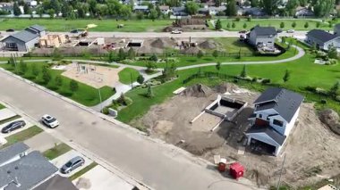 İnşaatı devam eden bir evi olan bir yerleşim yeri. Sokak evlerle dolu ve cadde boyunca birkaç araba park halinde.