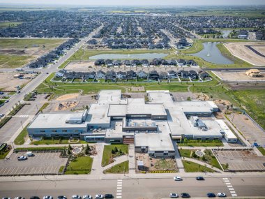 Önünde park yeri olan büyük bir okul binası. Otopark arabalarla dolu ve etrafta dolaşan bir sürü insan var.