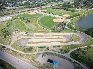 Toprak pisti ve beyzbol sahası olan bir park. Park evler ve bir yol ile çevrili.