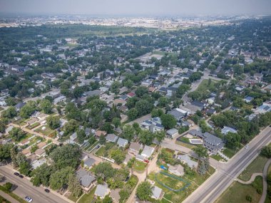 Şehir manzarası yukarıdan, evler ve mavi bir tabela. Evlerin çoğu beyaz ve gökyüzü bulutlu.