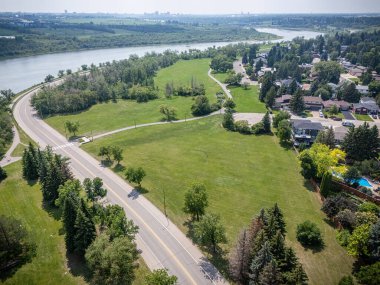 Arka planda nehir ve yeşil alan olan bir yol. Yol boş ve gökyüzü bulutlu.