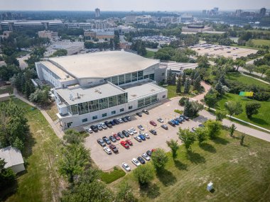 Altında park yeri olan büyük bir bina. Otopark birkaç kamyon da dahil olmak üzere arabalarla dolu. Bina ağaçlarla çevrili ve o bir spor salonu.