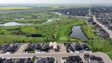 Golf sahası bir yerleşim yerinin arka planında gösterilir. Evlerin hepsi düzgünce dizilmiş ve caddeye park edilmiş birkaç araba var.