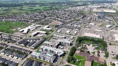 Şehir manzarası ve ortasında büyük bir bina. Şehir hareketlilikle dolup taşıyor. Gökyüzü açık ve güneş parlıyor.