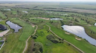 Göllü golf sahası ve arka planda evleri var. Golf sahası çitlerle çevrili ve ona giden bir yol var.