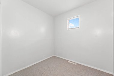 Penceresi ve beyaz duvarı olan küçük bir oda. Oda boş ve minimalist bir görünüşü var.