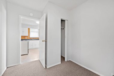 Beyaz kapısı ve beyaz duvarı olan küçük, boş bir oda. Oda boş ve dağınık.