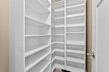 Rafları ve kapısı olan beyaz bir kiler. Kiler boş ve temiz. Kilerin beyaz rengi ona parlak ve temiz bir görünüm veriyor.