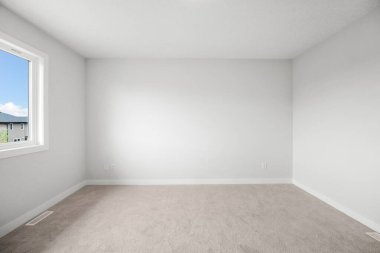 Penceresi ve duvarı olan beyaz bir oda. Oda boş ve minimalist bir görünüşü var.