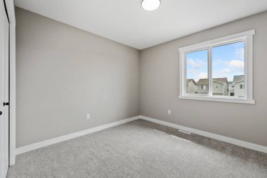 Beyaz duvarı ve penceresi olan bir yatak odası. Oda boş ve minimalist bir görünüşü var.