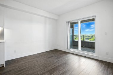 Şehre bakan geniş pencereli, geniş, açık bir oturma odası. Oda boş ve minimalist bir havası var.