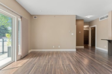 Büyük, açık bir oturma odası, bronzlaşmış bir duvar ve ahşap zemin. Oda boş ve minimalist bir görünüşü var.